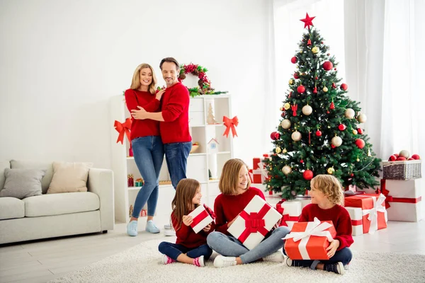 Foto van volle grote familie vijf mensen ontmoeten drie kleine kinderen houden geschenken lint boog nieuwsgierig ouderschap x-mas boom dragen rode trui jeans in huis woonkamer veel aanwezig dozen binnen — Stockfoto