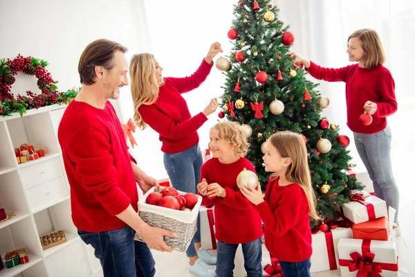 Photo of full big family five people meeting three little kids decorate x-mas tree dad help son daughter hold ball wear red jumper jeans in home living room presents mistletoe indoors Stock Image