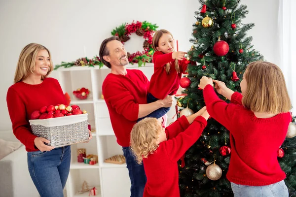 Foto van volledige grote familie vijf mensen verzamelen van drie kleine kinderen versieren x-mas boom moeder glimlach brengen doos kleurrijke speelgoed slinger lichten dragen rode trui jeans in huis woonkamer binnen — Stockfoto