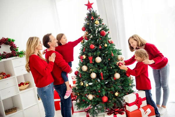 Фото большой семьи пять человек, встречающихся с тремя маленькими детьми папа держать дочь сестра помочь брату украсить рождественские елки игрушки шары звезда носить красные джинсы свитер в доме гостиной в помещении — стоковое фото