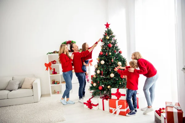 Foto av hela stora familjen fem personer samla tre små barn pappa hålla hjälp dotter dekorera x-mas träd tinsel grannlåt stjärna bära röda jumper jeans i hemmet vardagsrum presentförpackning inomhus — Stockfoto