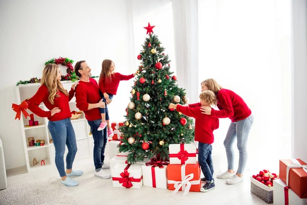 Foto van volledige grote familie vijf mensen ontmoeten drie kleine kinderen vader houden dochter versieren x-mas boom speelgoed ballen ster dragen rode trui jeans in huis woonkamer cadeau dozen binnen — Stockfoto