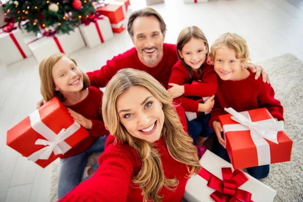 Photo of full big family five people gathering three small kids sit floor hold present box mom make shoot selfie wear red jumper in living room x-mas tree lights many gifts indoors