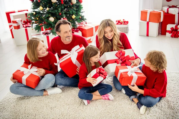 Foto van het hele gezin vijf mensen ontmoeten drie kleine kinderen zitten vloer houden grote geschenkdoos uitpakken dragen rode trui jeans in woonkamer x-mas boom slinger vele geschenken binnen — Stockfoto