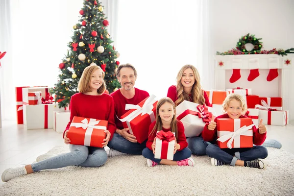 Fotografie plné velké rodiny pět lidí setkání tři malé děti sedět koberec podlaha hold dárky chlapec show thumb-up oblečení červená jumper v obývacím pokoji x-mas strom věnec dárkové krabice uvnitř — Stock fotografie