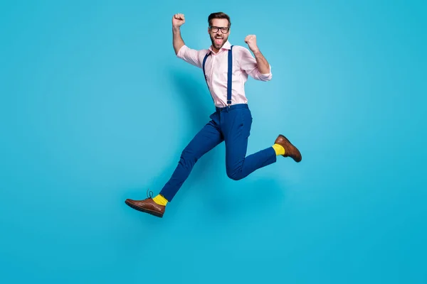 Πλήρης φωτογραφία προφίλ του σώματος του όμορφου άνδρα άλμα ψηλά στο τρέξιμο εργαζόμενος εργασίας ανταγωνισμού αυξήσει γροθιές πρώτη θέση νικητής φορούν specs πουκάμισο τιράντες παντελόνι μπότες απομονωμένο μπλε χρώμα φόντο — Φωτογραφία Αρχείου