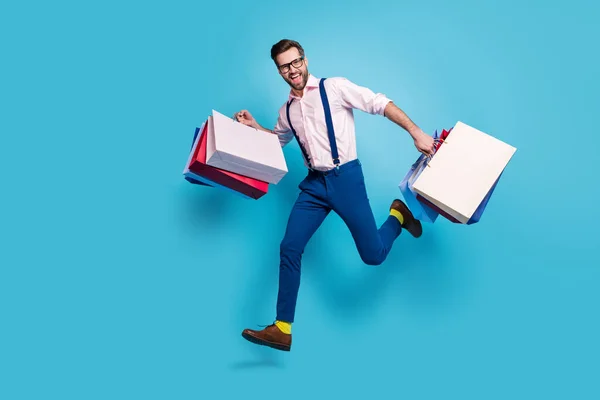 Pełna długość profil zdjęcie przystojny biznes człowiek nosić torby skakać wysoki zakup wakacje rzeczy centrum handlowe sklep centrum handlowe nosić okulary koszulka szelki spodnie buty odizolowany niebieski kolor tło — Zdjęcie stockowe
