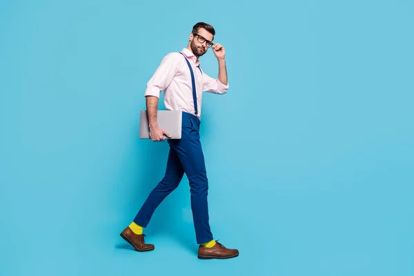 Full size profile photo of handsome confident guy carry notebook walk corporate meeting office successful worker wear specs shirt suspenders pants footwear isolated blue color background