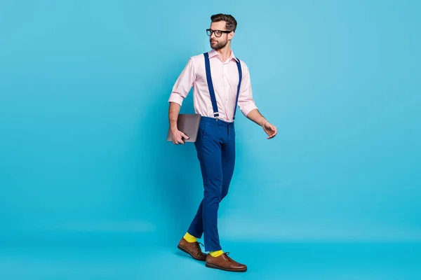 Full size zdjęcie przystojny pewny biznes facet trzymać komputer spacer spotkanie biuro sukces szef szef pracownik nosić specs koszulka szelki spodnie obuwie odizolowany niebieski kolor tło — Zdjęcie stockowe