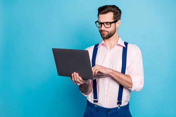 Foto de hombre de negocios machista guapo moda ropa chico uso de las especificaciones de visión de la vista reloj trabajando con la computadora estancia en casa desgaste camisa rosa tirantes pantalones aislados color azul fondo — Foto de Stock