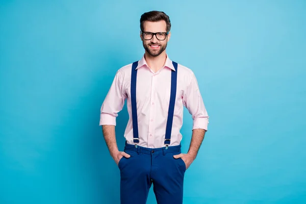 Φωτογραφία του όμορφος macho επιχειρήσεων άντρας τάση ρούχα τύπος ακτινοβολούν toothy χαμόγελο όραση specs χέρια στις τσέπες φορούν ροζ πουκάμισο τιράντες παντελόνι απομονωμένο παστέλ μπλε χρώμα φόντο — Φωτογραφία Αρχείου