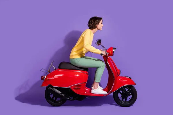 Teljes hossz testméret oldalsó profil fotó fiatal lány visel alkalmi ruhát vezetés piros motorkerékpár mosolygós várakozással elszigetelt élénk lila színű háttér — Stock Fotó