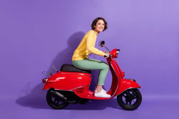 Full length body size profile photo of brunetka ładna student jazdy retro czerwony motorower uśmiechając się szczęśliwie odizolowany na jasnofioletowy kolor tła — Zdjęcie stockowe