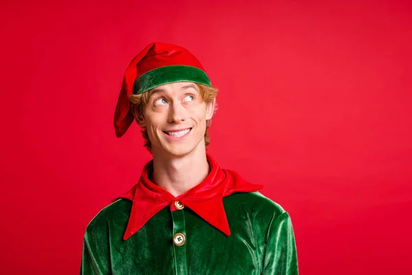 Фото положительного парня искать пустое пространство сияющие блестящие улыбки носить Санта-Эльф зеленый костюм головной убор красный цвет фона — стоковое фото