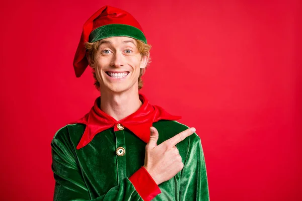 Photo of positive elf guy point finger empty space x-mas christmas ads wear costume cap isolated on bright red color background