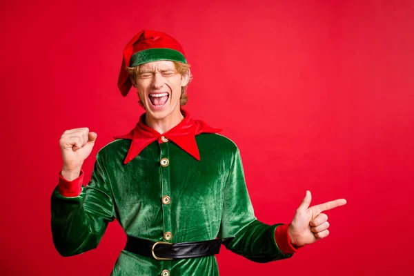 Foto von erfreut Elf Kerl Zeigefinger Copyspace Weihnachten Anzeigen heben Fäuste isoliert auf rotem Glanz Farbe Hintergrund — Stockfoto