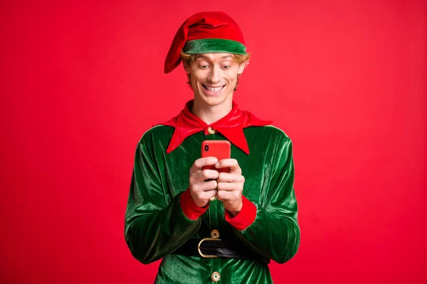 Küçük çılgın elf 'in fotoğrafı, akıllı telefondan selamlama okunuyor, başlık giyiliyor, parlak kırmızı arka planda izole edilmiş. — Stok fotoğraf