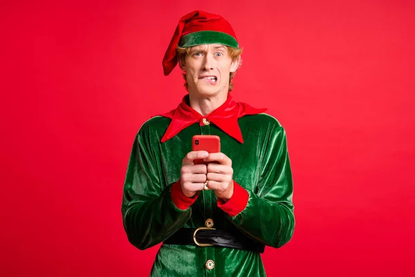 Різдвяна вечірка на Різдво скасувала фанкі хлопець ельф відчуває себе страшно тримати смартфон укус зубів губи ізольовані на червоному тлі — стокове фото