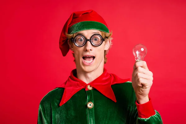 Kreative Gedanken. Aufgeregt verrückte Elf halten Glühbirne tragen grüne Mütze Kostüm isoliert auf rotem Glanz Farbe Hintergrund. — Stockfoto
