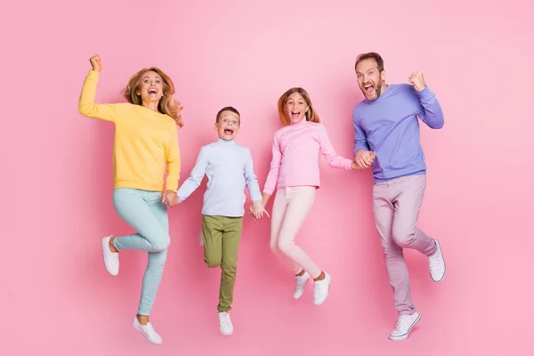 Pełna długość zdjęcie ekstatycznej mamusi tatuś małe dzieci skakać trzymać się za ręce podnieść pięści izolowane na pastelowym tle kolor — Zdjęcie stockowe