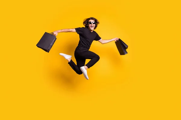Ganzkörpergröße Porträt des Mannes springt auf halten Pakete nach dem Verkauf am schwarzen Freitag isoliert auf leuchtend gelben Hintergrund — Stockfoto