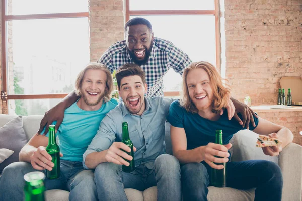 Cuatro personas mejores amigos hombres sentarse sofá celebrar pinta bebida botella disfrutar de tiempo libre viendo película película celebrar pizza rebanada en casa en interiores — Foto de Stock