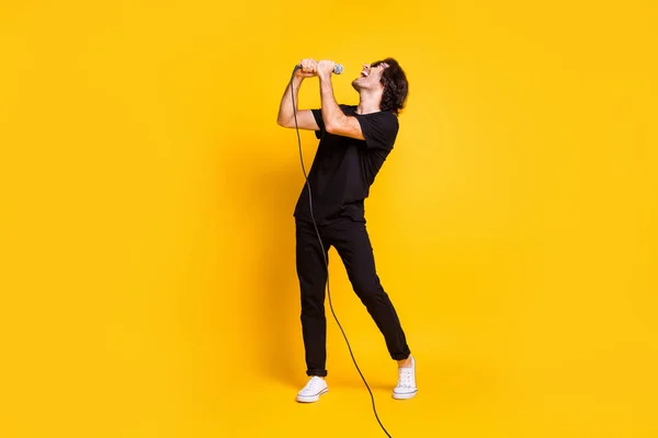 In voller Länge Profilfoto des jungen Mannes halten Mikrofon singen offenen Mund tragen schwarze T-Shirt Hose weiße Turnschuhe Brille isoliert gelbe Farbe Hintergrund — Stockfoto