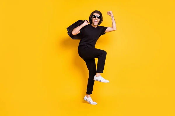 In voller Länge Foto des jungen Mannes halten Einkaufspakete offenen Mund tragen schwarze T-Shirt Hose weiße Turnschuhe Sonnenbrille isoliert gelbe Farbe Hintergrund — Stockfoto