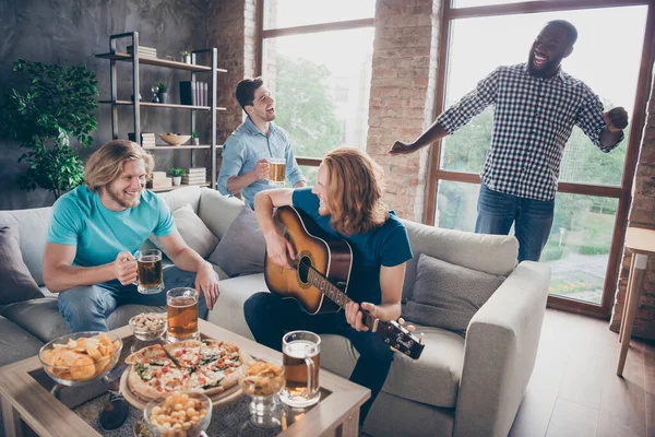 네 명의 친구들은 실내에서 즐거운 집 생활을 하고 있습니다. 아늑 한 소파에 앉아 있는 금발의 남자 팝 스타, 기타를 치고 있는 미국 남자 — 스톡 사진