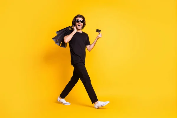 Full längd foto av ung man steg håll mall paket bära svart t-shirt byxor vita sneakers glasögon isolerad gul färg bakgrund — Stockfoto