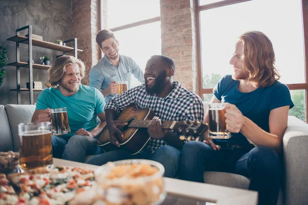 Cuatro hombres mejores biddies divertirse día de fiesta celebrar sentarse sofá afroamericano tocar guitarra melodía chicos escuchar celebrar pinta bebida taza disfrutar en casa en interiores — Foto de Stock