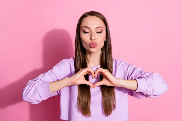 Foto de atraente bonita senhora olhos fechados mãos mostrar coração símbolo expressar sentimentos cardíacos romântico data enviar beijos de ar namorado usar camisola roxa isolado cor pastel rosa fundo — Fotografia de Stock