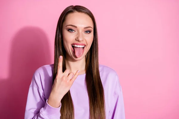 Photo of attractive funky cool youth lady protruding tongue out mouth show finger horns crazy rocker music lover wear casual purple sweater isolated pink pastel color background