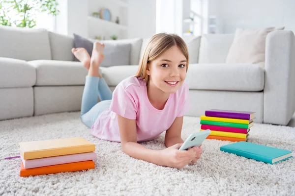 Ganzkörperfoto von positivem Kind Mädchen Liegen Boden Teppich verwenden Handy genießen Social-Media-Kommunikation Gespräch repost abonnieren im Haus drinnen — Stockfoto