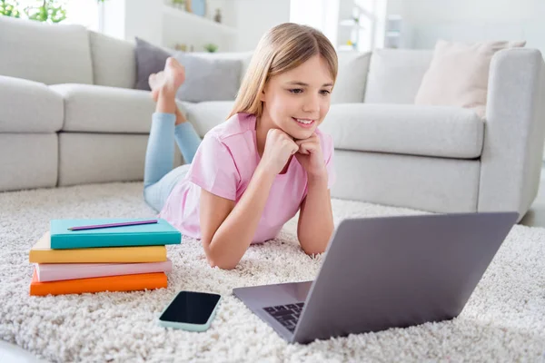 Foto de tamaño completo de niña niña positiva estudio remoto portátil reloj tutor educación webinar acostado alfombra de piso en casa en el interior — Foto de Stock
