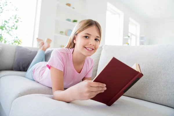 Great remote study concept. Full size photo of positive kid pupil girl lying comfy divan read interesting textbook prepare school project in house indoors — Stock Photo, Image