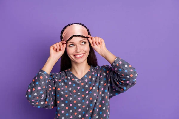 Foto di positivo allegro ragazza toccare mano occhio maschera guardare copyspace usura punteggiato pigiama isolato su viola viola colore sfondo — Foto Stock