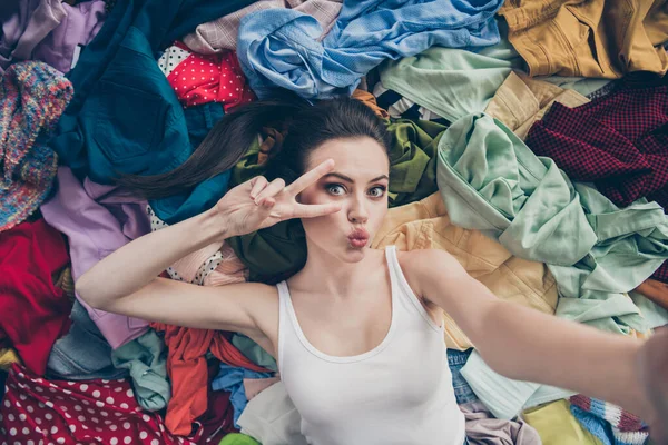 Alto ángulo por encima de la foto de la señora encantadora casa limpieza de primavera acostado muchas prendas de vestir piso preparado cosas desordenadas lavado hacer selfies mostrar v-signo símbolo seguidores sus cosas envían beso en el interior —  Fotos de Stock