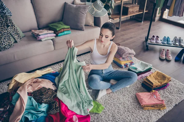 Top above high angle view photo of focused volunteer girl sit floor carpet arrange her used clothes decide what she will give charity in house indoors