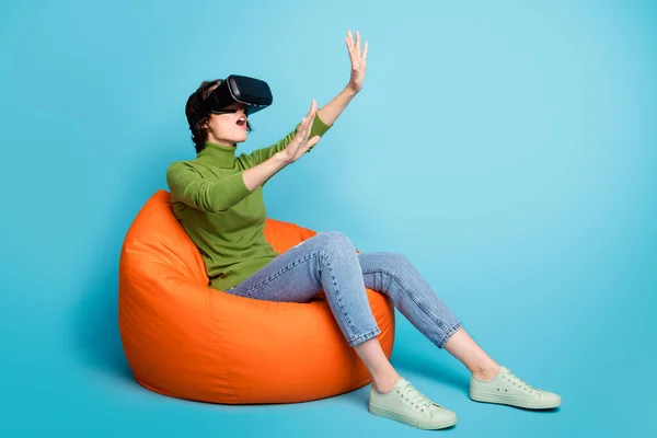 Full body profil boczny zdjęcie wstrząśnięty dziewczyna siedzieć fasola krzesło mają gogle grać czujnik vr-box gra trzymać ręka copyspace nosić zielony sweter dżinsy odizolowany niebieski kolor tło — Zdjęcie stockowe