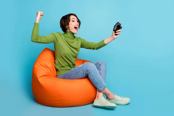 喜びの女の子の完全な長さの写真豆の椅子プレイビデオゲームは拳を上げるレーススピード競争の摩耗スタイルスタイリッシュなトレンディーなセーター孤立青の色の背景 — ストック写真
