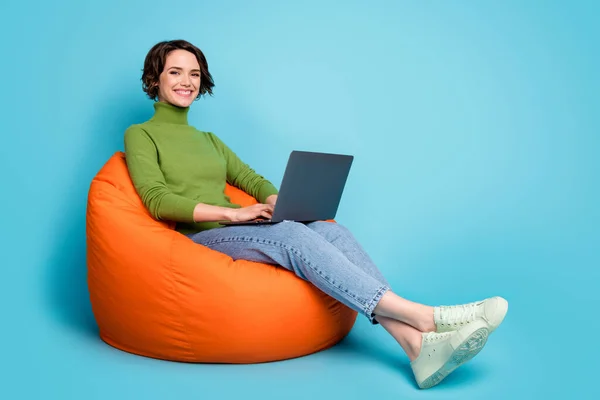 Foto samping penuh gadis positif duduk kursi kacang menggunakan laptop menikmati komunikasi online memakai gaya hijau trendi jins terisolasi warna biru latar belakang — Stok Foto