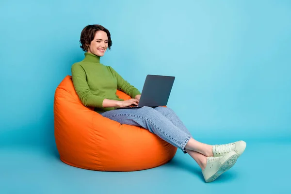 Foto samping penuh gadis positif duduk kursi kacang menggunakan teknologi komunikasi laptop memakai gaya trendi penarik denim latar belakang warna biru yang terisolasi — Stok Foto