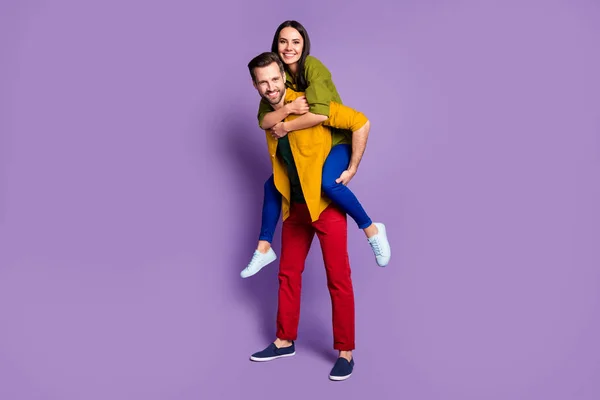フル長さの写真かなり女性ハンサムな男カップル運ぶピギーバック遊び心ムード過ごす時間隔離着用カジュアル明るいシャツパンツシューズ服隔離された紫の色の背景 — ストック写真