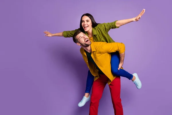 Foto vrij grappig dame knap man paar dragen piggyback voldoen aan avonturen speelse gespreide armen als vleugels dragen casual shirts broek schoenen geïsoleerd paars kleur achtergrond — Stockfoto