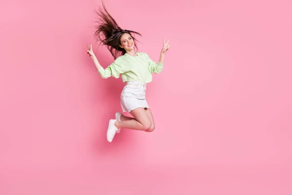 Full längd profil foto av attraktiv ung dam hoppar högt visar v-tecken symboler bära casual gröda pullover naken mage kjol skor isolerad rosa färg bakgrund — Stockfoto