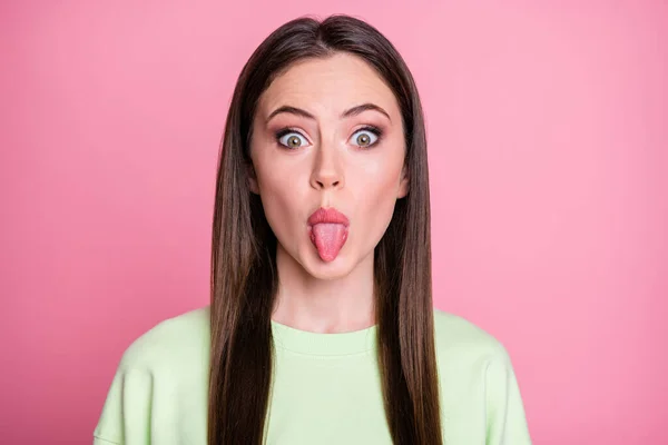Closeup photo of funny crazy lady straight long hairdo funny girlish sticking tongue out mouth playful foolish mood wear casual green sweatshirt pullover isolated pink color background