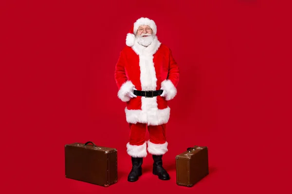 Foto de comprimento total de Papai Noel barba cinza mãos quadris bagagem desgaste x-mas traje casaco cinto óculos luvas botas de couro óculos isolado cor vermelha fundo — Fotografia de Stock