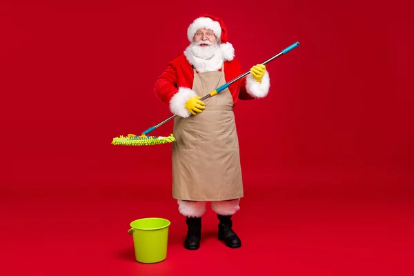 Pełna długość zdjęcie Santa Claus szara broda trzymać mop nosić x-mas kostium fartuch płaszcz czapka okulary gumowe rękawice skórzane buty okulary izolowane czerwony kolor tło — Zdjęcie stockowe