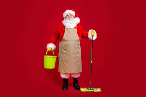 Pełna długość zdjęcie Santa Claus szara broda trzymać mop wiadro nosić x-mas kostium fartuch płaszcz nakrycie głowy okulary lateks rękawice buty okulary izolowane czerwony kolor tło — Zdjęcie stockowe